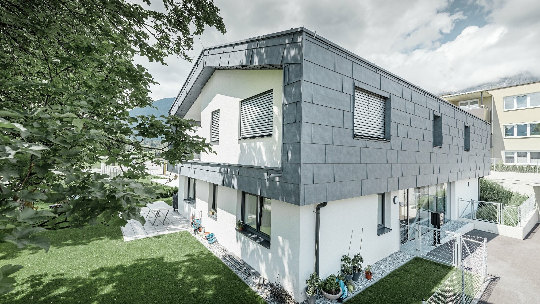 Moderne Aufstockung eines Wohnhauses mit flachem Satteldach und ohne Dachvorsprung; Die Fassadenverkleidung wurde mit dem PREFA Fassadenpaneel FX.12 in Steingrau.