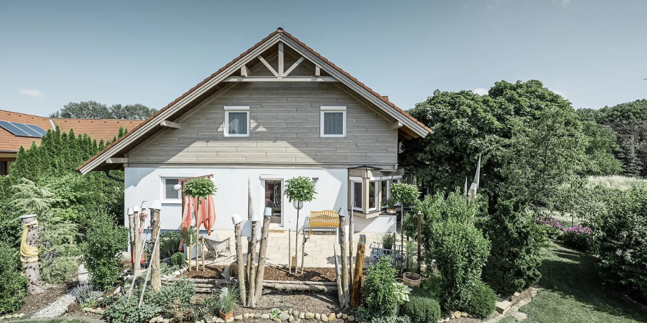Maison individuelle rénovée avec un nouveau revêtement de pignon dans un style bois moderne gris-beige, combiné à une façade crépie, un toit en pente et un jardin bien entretenu.