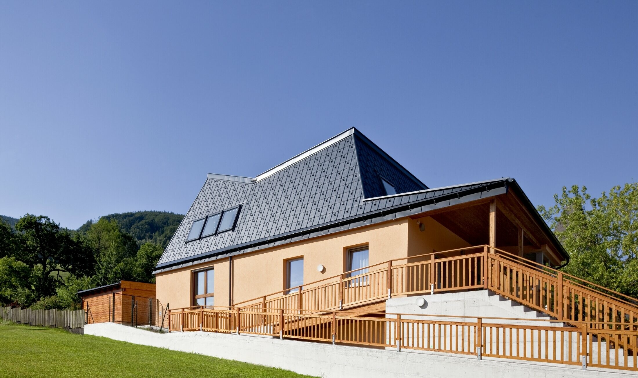 Maternelle avec façade en crépi orange et toiture à pans inclinés, recouverte de tuiles PREFA P.10 anthracite ;