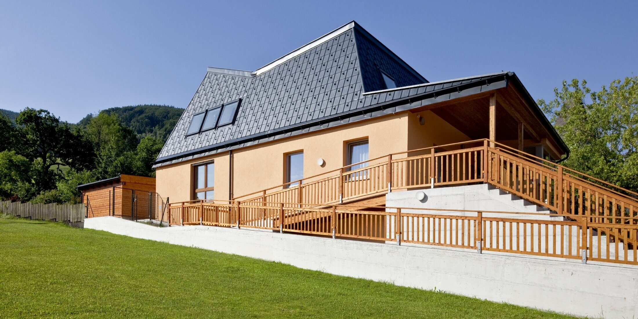 Kindergarten mit oranger Putzfassade und verwinkeltem Dach, gedeckt mit der PREFA Dachplatte in P.10 Anthrazit;