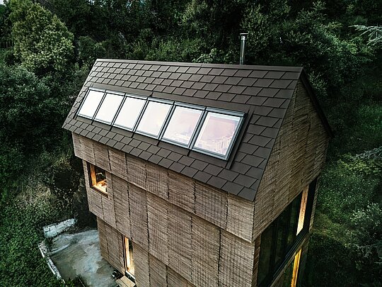 Vue du toit d'une maison avec des bardeaux PREFA de couleur P.10 brun noisette et des puits de lumière intégrés, entourée du paysage naturel de l'ouest de la France.