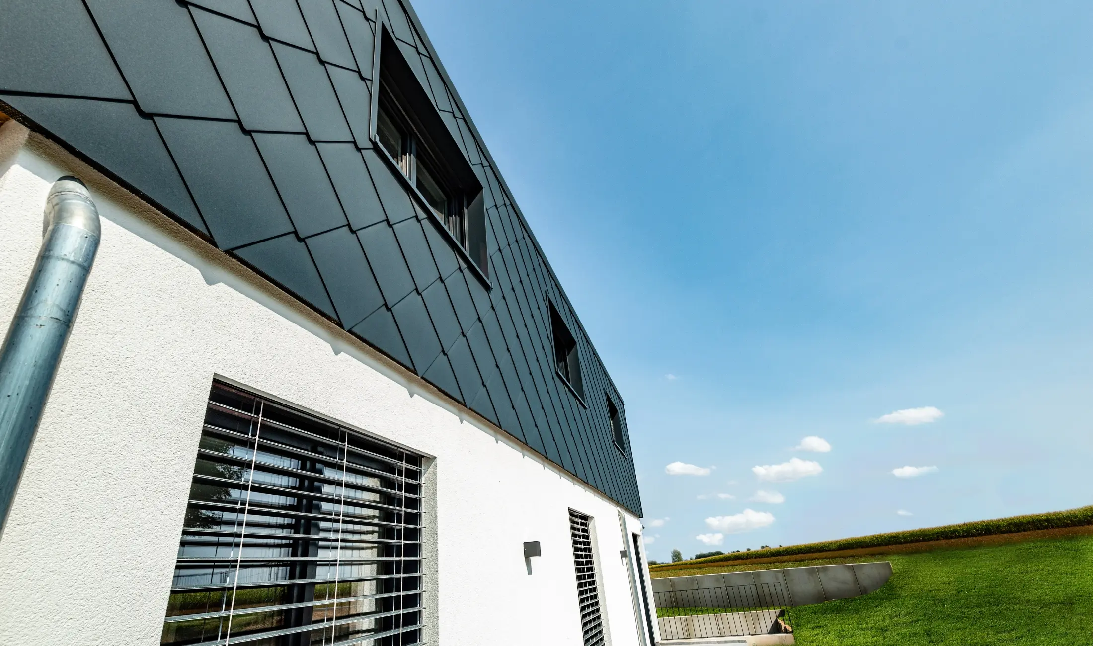 Losange de façade PREFA grand format de 44 cm couleur anthracite combiné avec une façade revêtue de crépi blanc.