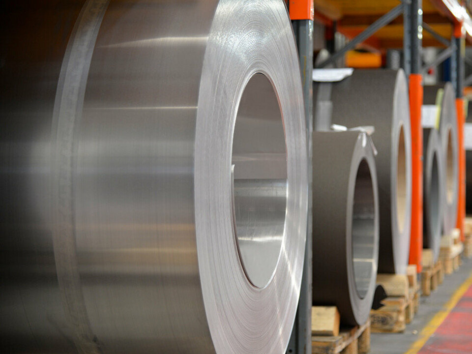 Bobines d’aluminium ("coils") sur palettes en bois : au premier plan, un rouleau en aluminium naturel et derrière, d’autres bandes et feuilles d’aluminium.
