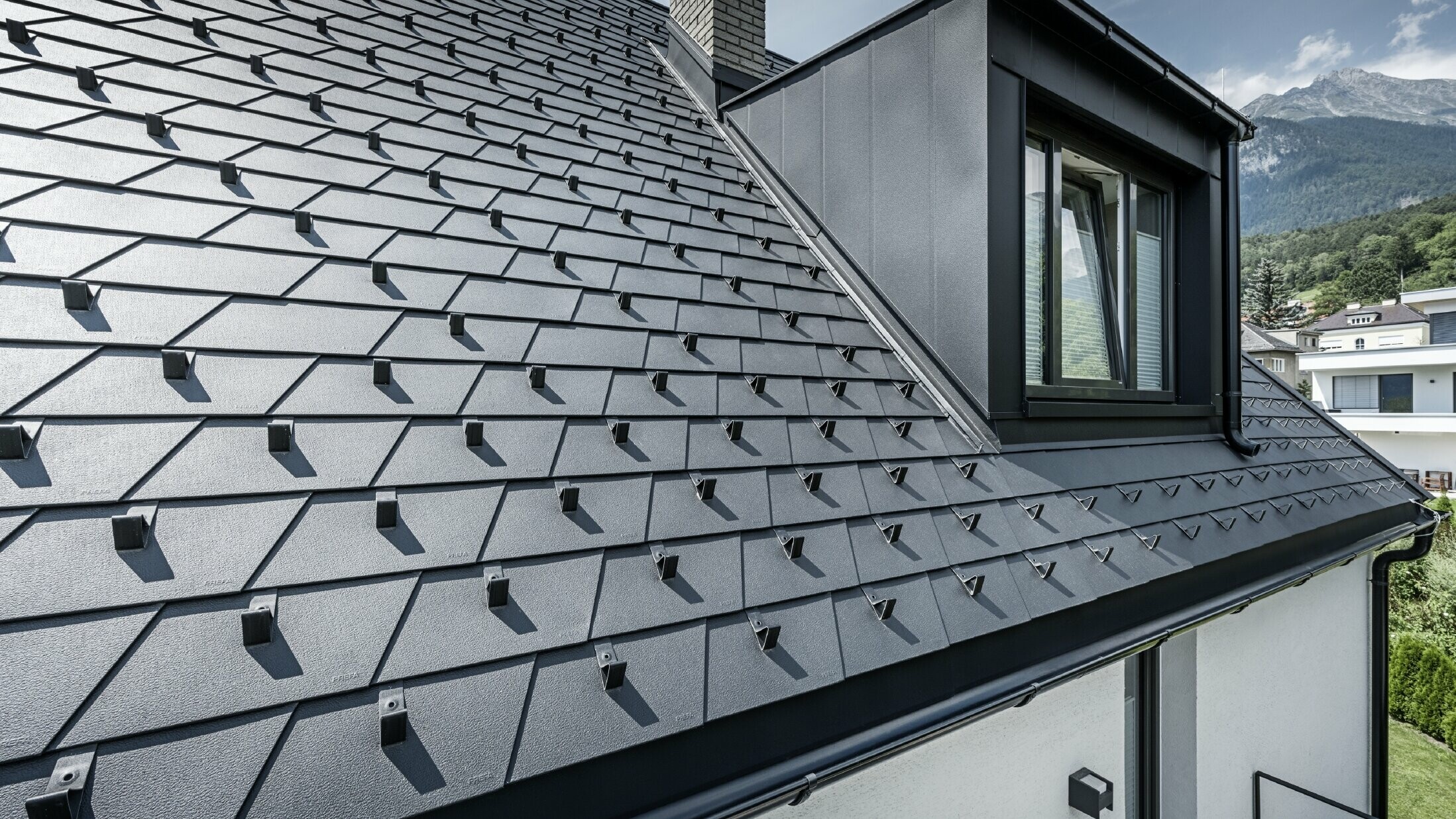 Detaillierte Aufnahme eines Daches mit Gaube und Fenster, auf der Dachfläche sind PREFA Dachschindeln in Schwarz mit Schneestoppern verlegt.