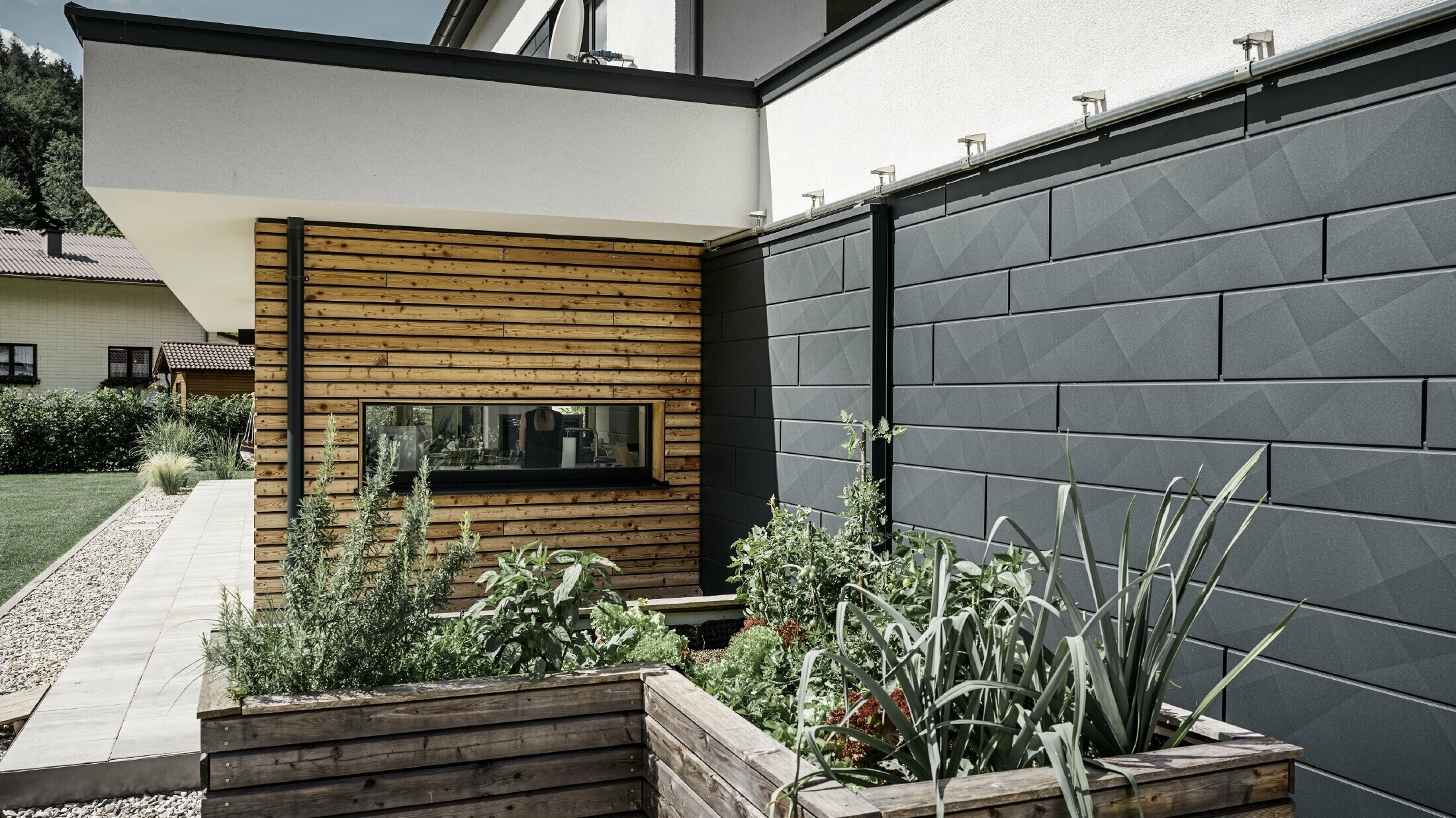 On voit à droite les panneaux de façade Siding.X et à gauche une partie de la façade en bois. Une plate-bande surélevée est visible au premier plan.