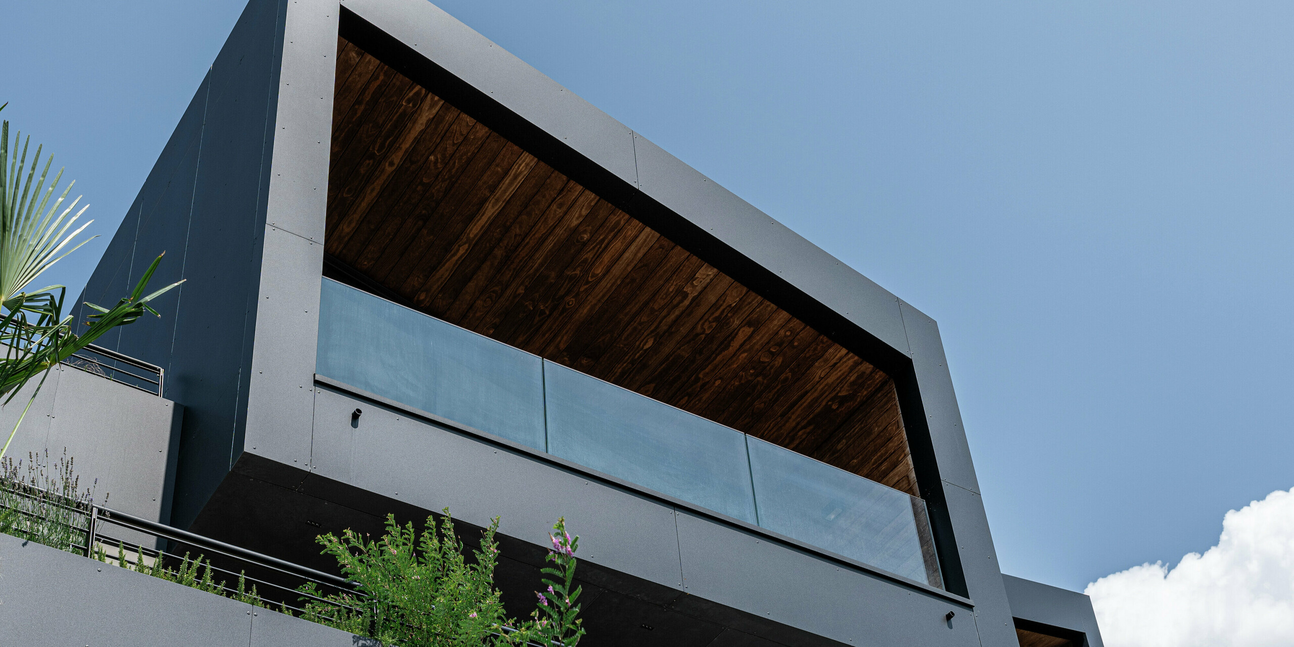 Moderne Architektur trifft auf langlebige Materialien: Die minimalistische Kubusform mit Pultdach und markanter, überdachter Terrasse wird durch die robuste PREFA Aluminiumfassade in P.10 Schwarz perfekt in Szene gesetzt. Die Untersicht betont die klaren Linien und die Widerstandsfähigkeit des Materials, die integrierte Begrünung sorgt für natürliche Harmonie. Witterungsbeständig, pflegeleicht und stilvoll - die PREFA Gebäudehülle garantiert Schutz und Beständigkeit in jeder Situation.