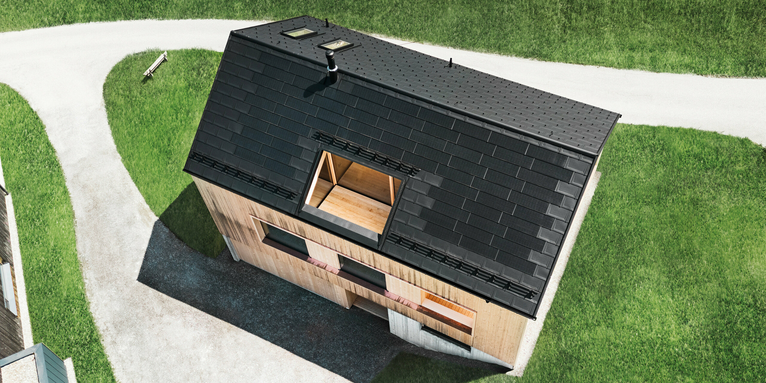 Prise de vue par drone avec vue aérienne d'une maison familiale écologique à Egg, qui se distingue des pelouses vertes environnantes par son toit solaire PREFA noir et les R.16 traditionnels PREFA. Les modules solaires stratégiquement placés maximisent l'efficacité énergétique, tandis que la géométrie claire du toit et la façade en bois d'aspect naturel créent un lien entre la vie moderne et l'environnement rural. Cette maison incarne une conception progressive et respectueuse de l'environnement qui impressionne à la fois fonctionnellement et visuellement.