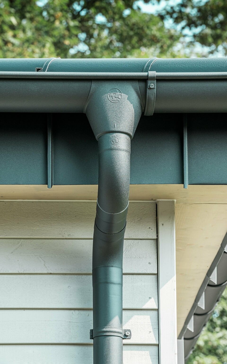 Nahaufnahme der robusten PREFA Dachentwässerung eines Bungalows in Rommerskirchen. Die hochwertige Saumrinne und das Ablaufrohr in P.10 Schwarz bieten optimalen Schutz vor Witterungseinflüssen. Langlebigkeit und Funktionalität verbinden sich hier mit elegantem Design aus Aluminium.