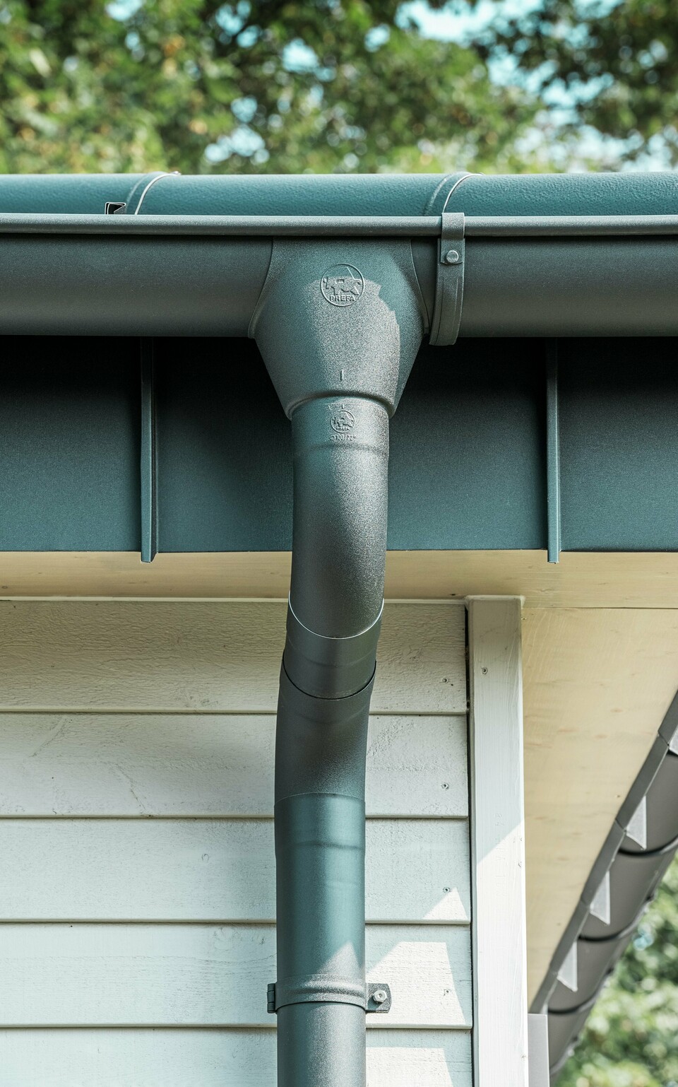 Gros plan du robuste système d'évacuation des eaux pluviales PREFA d'un bungalow à Rommerskirchen. La gouttière et le tuyau de descente de haute qualité P.10 noir offrent une protection optimale contre les intempéries. Durabilité et fonctionnalité se combinent avec un design élégant en aluminium.