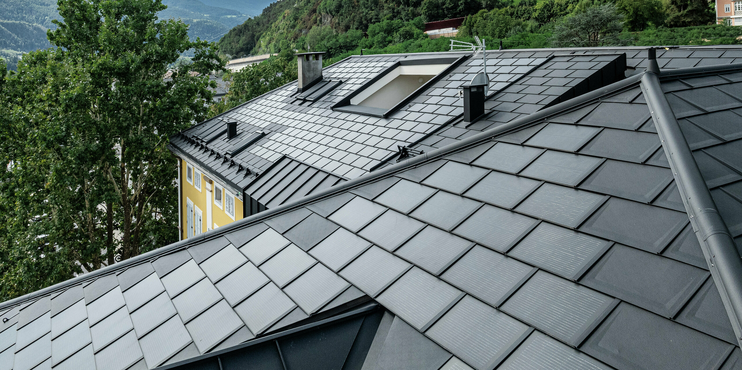 Vue détaillée du toit PREFA de l'hôtel Jarolim à Bressanone avec des tuiles solaires dotées de modules photovoltaïques intégrés, ainsi que des R.16 éprouvés. Le toit en aluminium durable combine une technologie innovante avec un design élégant et est idéal pour les bâtiments classés. Les modules photovoltaïques assurent une production d’énergie durable sans compromettre l’harmonie esthétique de la toiture. Robustesse, résistance aux intempéries et finition précise soulignent la qualité des produits PREFA.