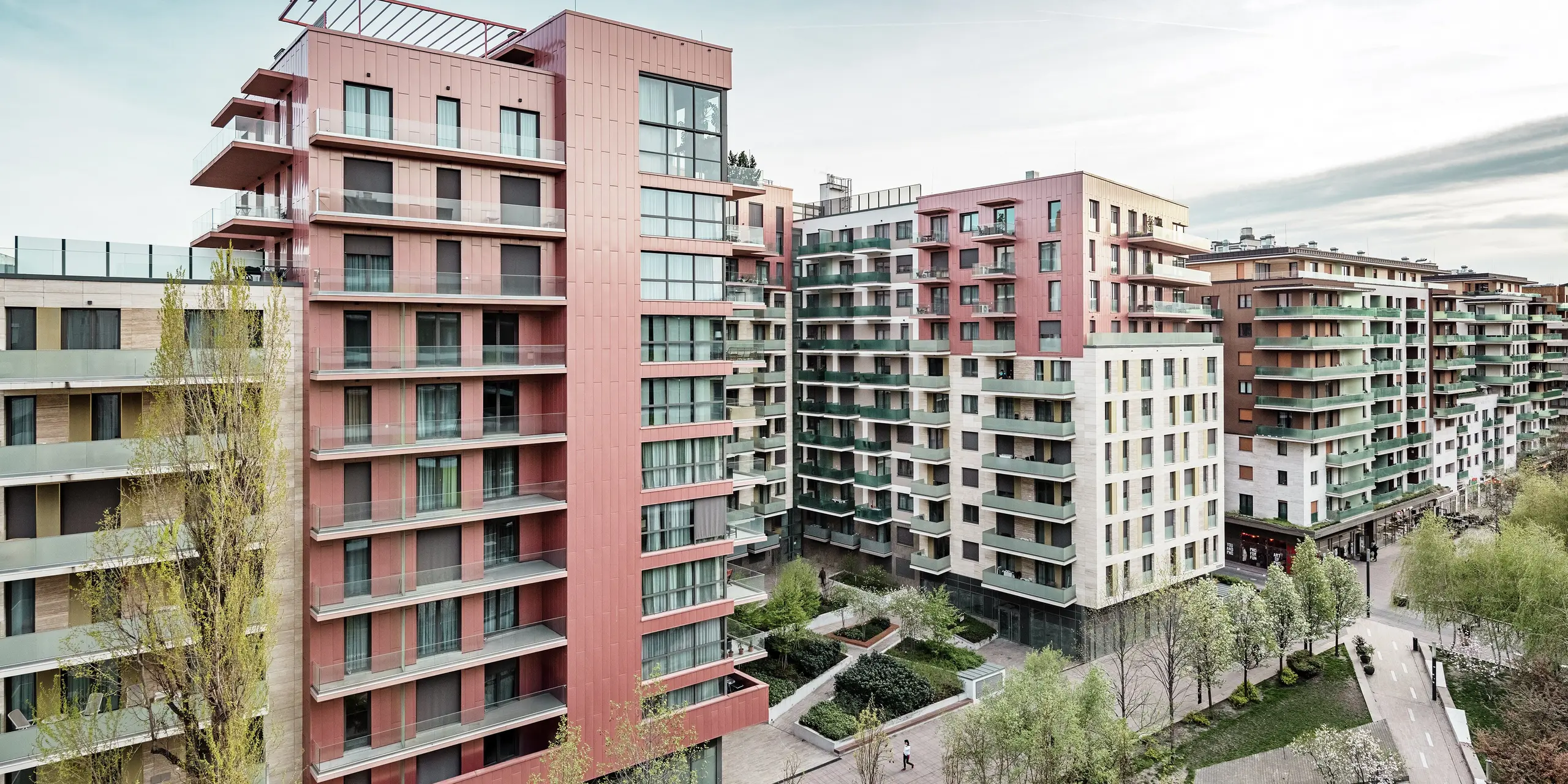 Vue panoramique du complexe résidentiel Grand Corvin, situé dans le nouveau quartier Corvin de Budapest. Les imposantes sections du bâtiment sont revêtues de plus de 800 m² de panneaux de façade Siding PREFA, posés verticalement et revêtus d'une finition saumon métallisée. Ce revêtement en aluminium durable crée des points forts architecturaux, s'intègre harmonieusement au tissu urbain et souligne le caractère contemporain et haut de gamme du nouveau complexe résidentiel situé le long de la promenade Corvin.