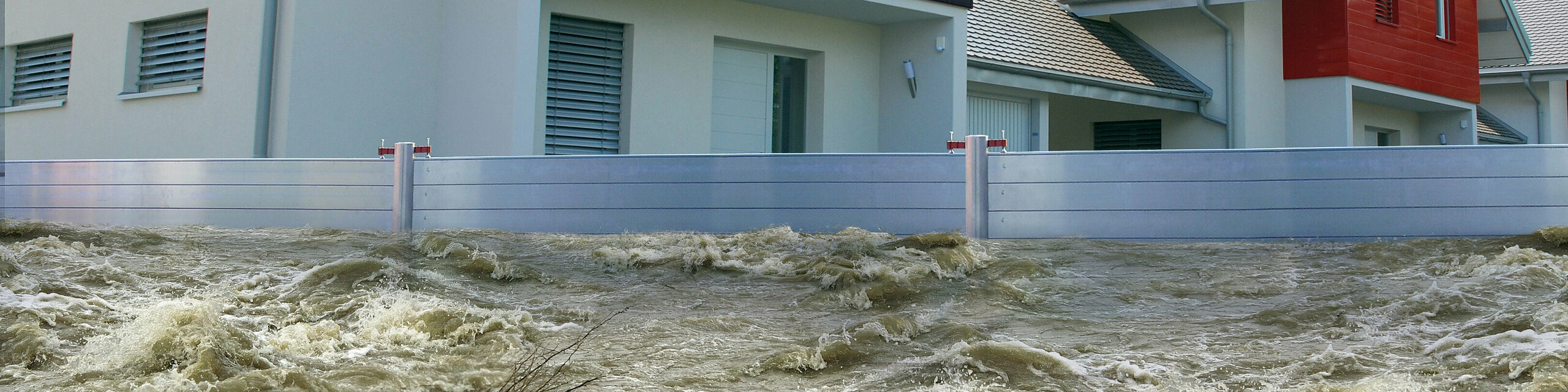 Auf dem Bild ist ein PREFA Hochwasserschutz zu sehen, der mehrere Häuser von großen Wassermengen schützt.