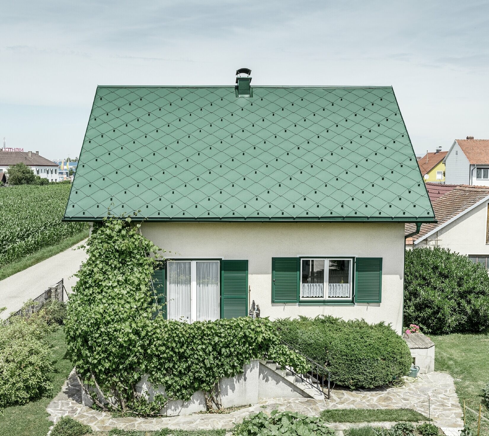 Toit à pignon de maison individuelle classique avec couverture en aluminium vert mousse et volets verts Le toit est recouvert de losanges de toiture PREFA 44 × 44 en P.10 vert mousse.