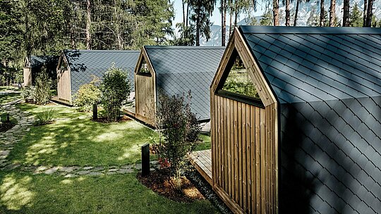 Au Secret Koi Garden, une série de mini-maisons minimalistes se nichent dans un écrin de verdure soigné, au bord du lac Natterer. Leurs toits et façades en pente sont revêtus de petits losanges en aluminium PREFA P.10 anthracite, créant une texture apaisante évoquant des écailles de poisson. Entourées d'arbres et d'arbustes, ces surfaces en aluminium PREFA, résistantes aux intempéries, offrent une protection optimale et confèrent à ce complexe de glamping une architecture épurée et intemporelle, en parfaite harmonie avec la nature.