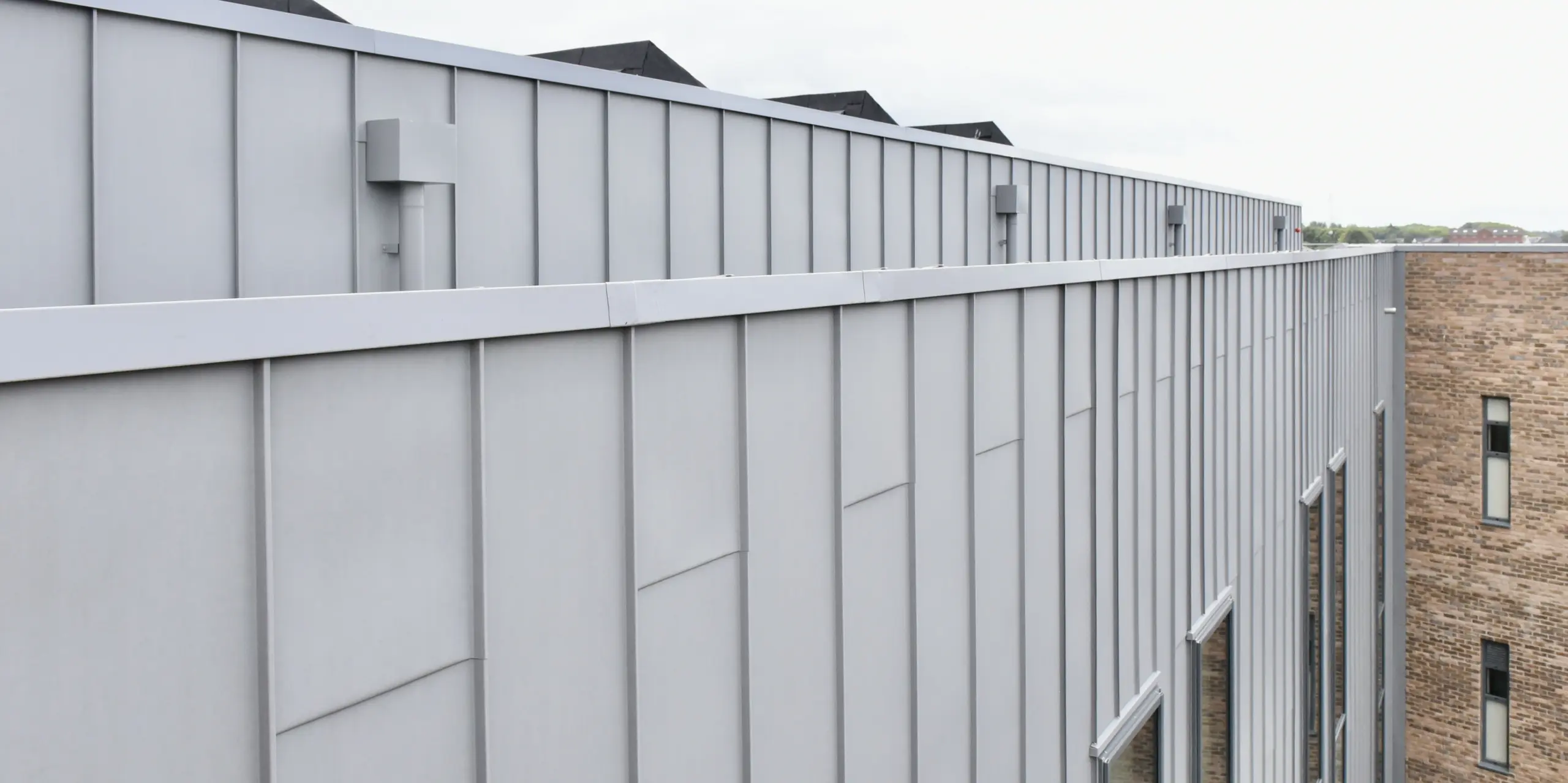 Vue détaillée de la façade en aluminium PREFALZ en gris quartz au Regional College North, Royaume-Uni. Les lignes claires et l'aspect mat du revêtement à joint debout soulignent la finition de haute qualité et le design intemporel.