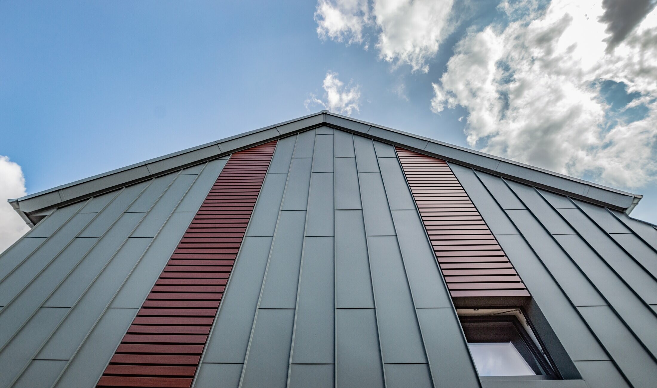 Vertikale Winkelstehfalzfassade mit Tafeldeckung in Hellgrau, sowie Siding horizontal in Holz dunkel von PREFA.