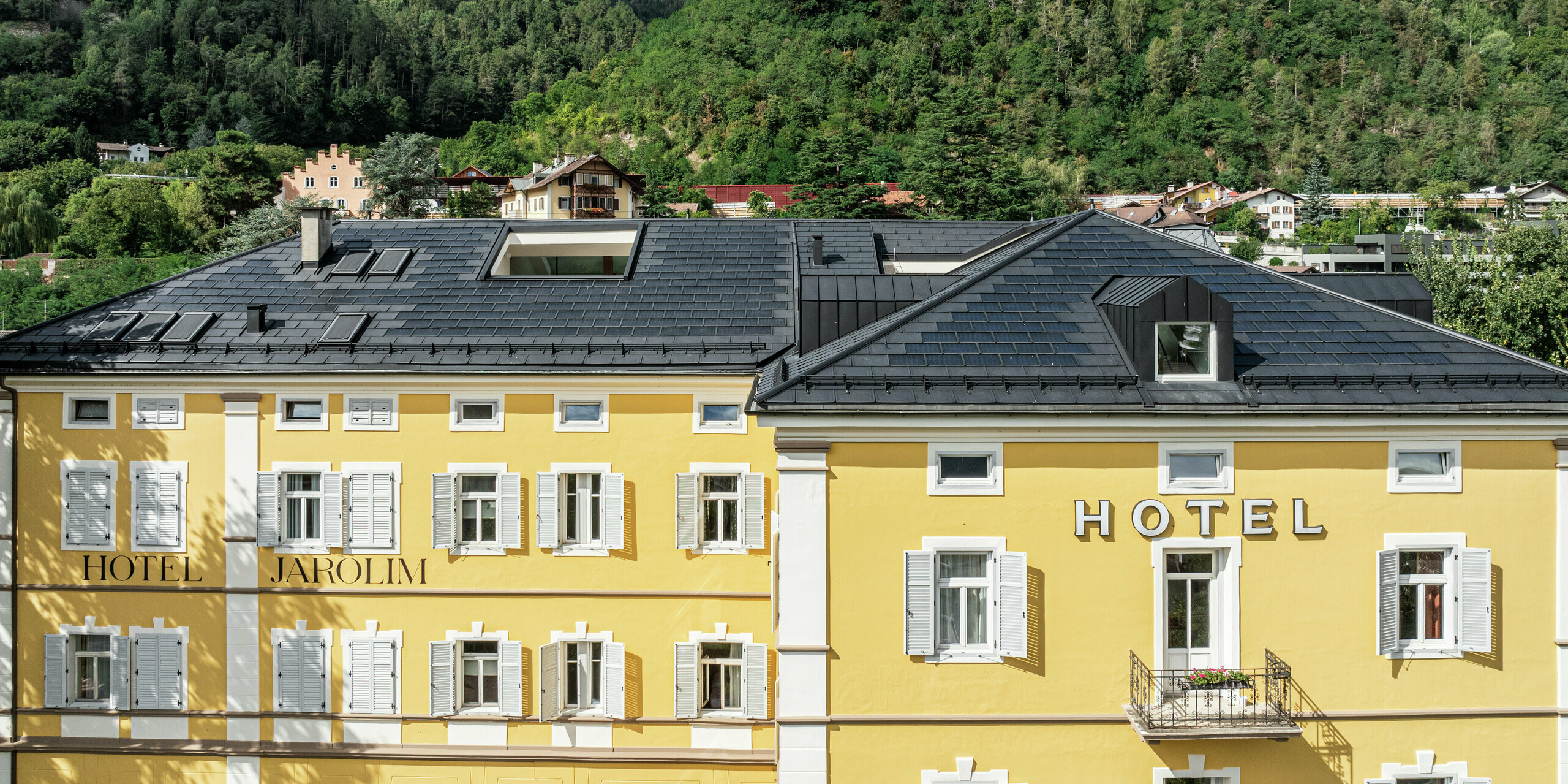 L'hôtel Jarolim à Bressanone présente son nouveau toit composé de tuiles solaires PREFA et de R.16 en P.10 noir intemporel. La solution de toiture allie robustesse, résistance aux intempéries et légèreté, idéale pour les bâtiments classés. Les modules photovoltaïques intégrés génèrent une électricité respectueuse de l’environnement sans compromettre l’aspect historique. Des lucarnes et des détails de toiture parfaitement ajustés soulignent la haute qualité de fabrication et la polyvalence esthétique des produits en aluminium PREFA.