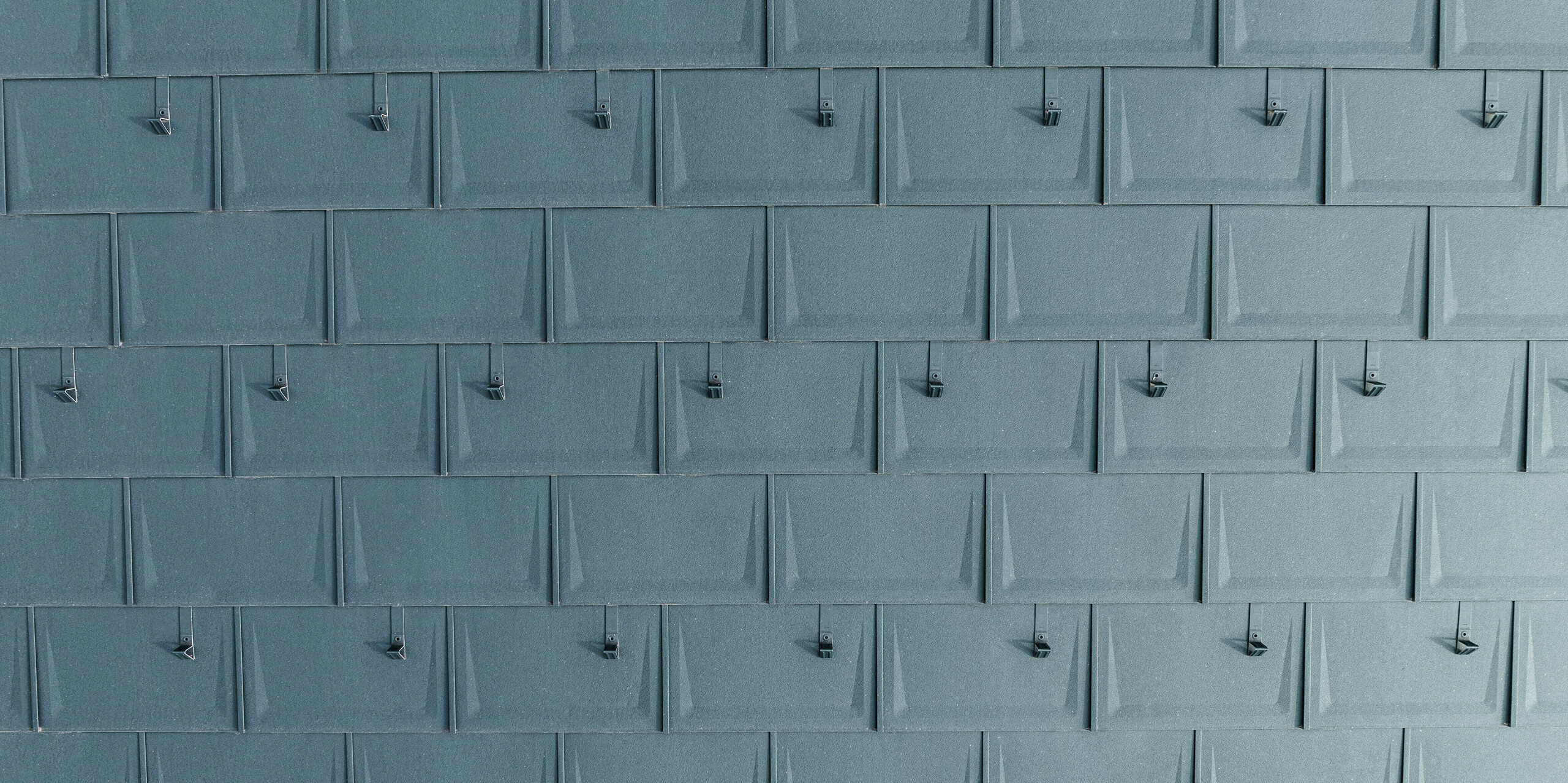 Detailansicht der präzise verlegten PREFA Dachplatten R.16 in P.10 Anthrazit mit montierten Schneestoppern. Die geradlinige Dachplatte aus Aluminium überzeugt durch moderne Optik, Langlebigkeit und extreme Witterungsbeständigkeit. Durch die ausgeklügelte Befestigungstechnik ist sie besonders sturm- und bruchsicher. Die Schneestopper sorgen für zusätzliche Sicherheit in schneereichen Regionen und verhindern ein unkontrolliertes Abrutschen der Schneemassen.