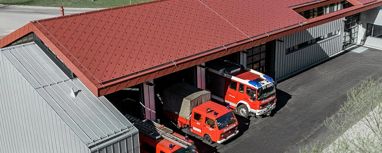 Véhicules de pompiers dans la caserne de la société PREFA. Le bâtiment est doté d’une toiture en losanges rouges (aluminium non inflammable) et d’une façade en aluminium.