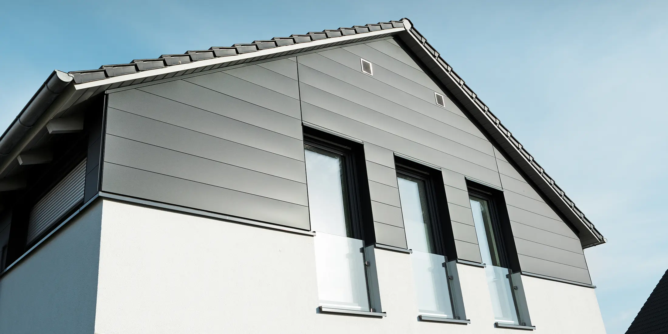 Moderne Hausfassade in Isenbüttel mit PREFA Sidings in P.10 Anthrazit – die Aluminiumverkleidung verleiht dem Einfamilienhaus einen eleganten und wetterfesten Look. Die vertikalen Fenster betonen die moderne Architektur zusätzlich.