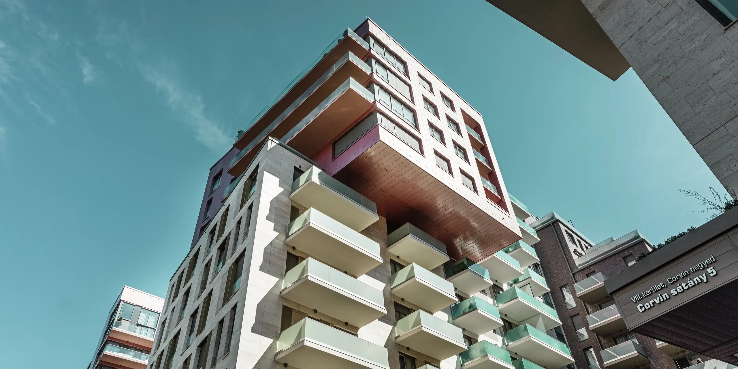 Vue aérienne saisissante du complexe résidentiel Grand Corvin, situé dans le quartier Corvin de Budapest, avec sa partie en porte-à-faux entièrement revêtue de panneaux de façade Siding PREFA d'une couleur saumon métallisé sur-mesure. L'installation verticale de cette façade en aluminium durable confère à ce bâtiment urbain moderne une structure élégante et met en valeur l'architecture de haute qualité dans le cadre d'un vaste programme de rénovation urbaine.