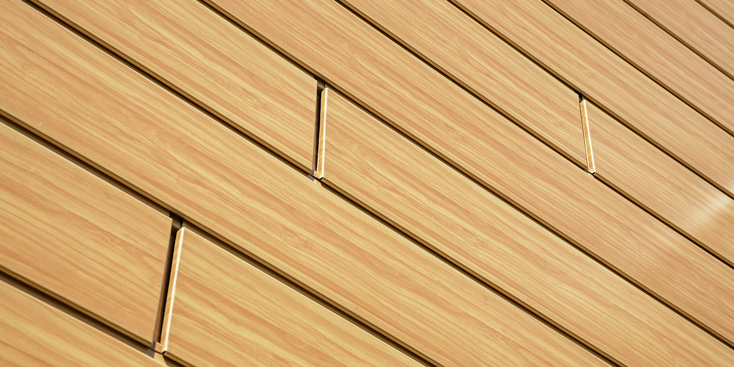 Nahaufnahme der PREFA Sidings in Eiche Natur. Die hochwertige Aluminiumverkleidung zeigt eine verblüffend echte Holzoptik mit feiner Maserung und warmem Farbton. Die präzise Linienführung der Paneele erzeugt eine moderne, ruhige Flächenwirkung und setzt den sanften Lichteinfall effektvoll in Szene. Die langlebigen PREFA Sidings sind witterungsbeständig, farbstabil und nahezu wartungsfrei – eine ästhetische und gleichzeitig funktionale Lösung für anspruchsvolle Fassadensanierungen.