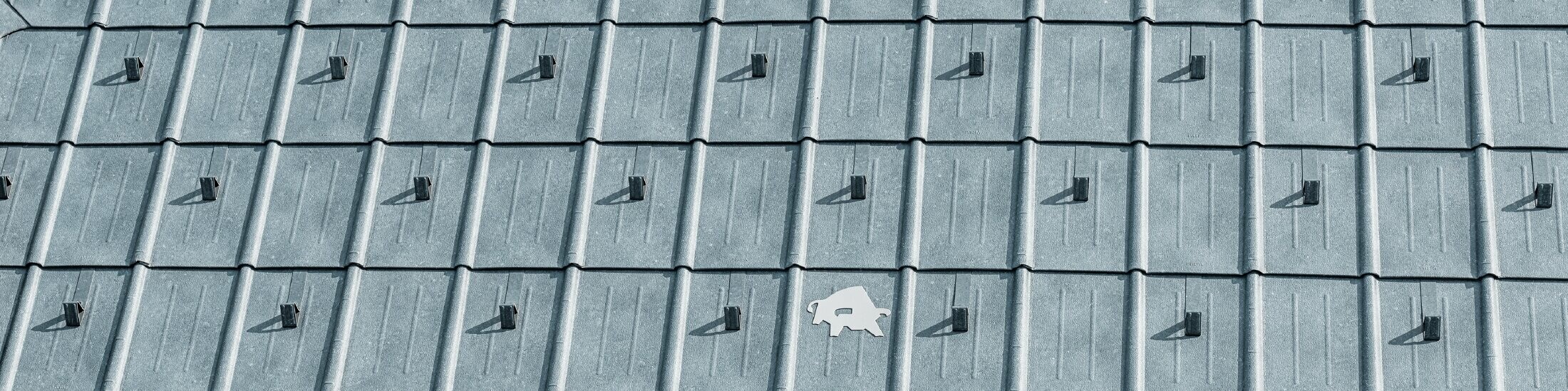 PREFA krovna ploča postavljena s PREFA logotipom bika u boji P.10 kamen-siva; krovna površina s PREFA limenim krovom.