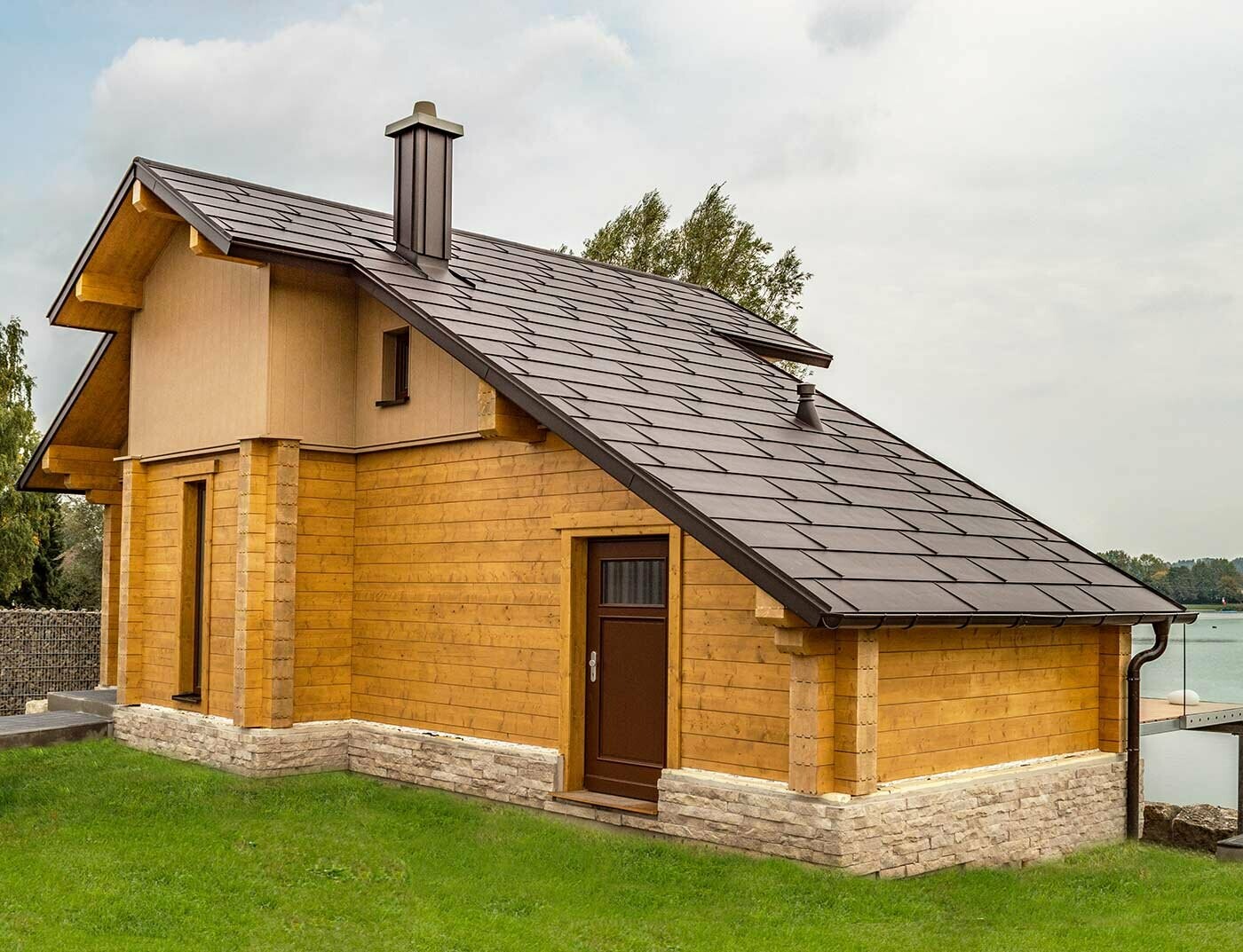 Maison au bord de l’eau recouverte de panneaux de toiture FX.12 PREFA couleur brun noisette ainsi que d’une façade couleurs brun sable et bois.