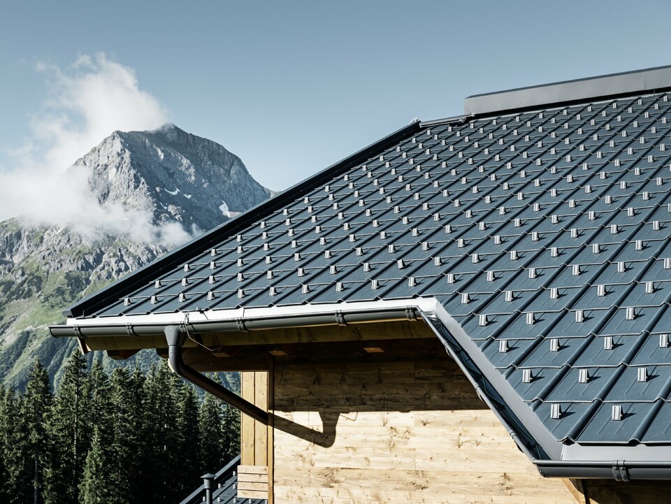 Maison en bois à la montagne, la toiture est recouverte avec la tuile PREFA couleur anthracite avec gouttière PREFA et façade en bois