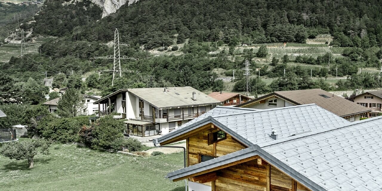 Vue aérienne du chalet Fabrice ; le chalet a été recouvert de tuiles R.16 PREFA couleur gris pierre avec arrêts neige, la partie haute du bâtiment est habillée avec une façade en bois rustique.