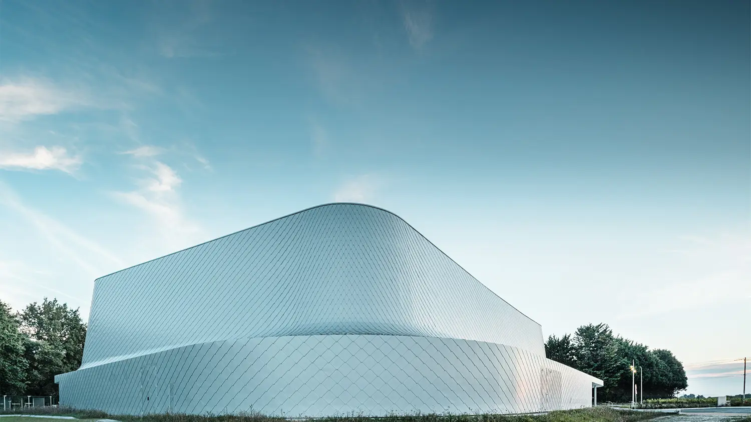 Hintere Seite der monochromen Halle mit Begrünung und einem angrenzenden Weg.