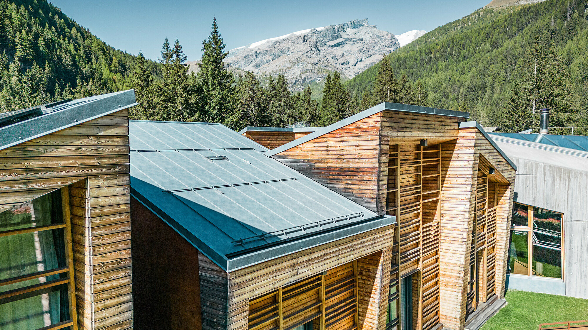 Seitliche Detailansicht der Dachlandschaft, die Holzfassade und die sorgfältig verlegten Prefalz Bahnen sind gut sichtbar.