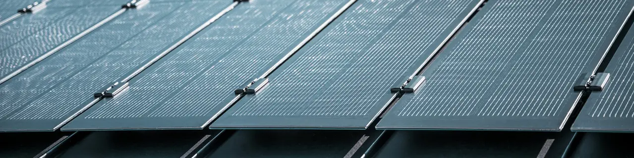 Montageansicht mehrerer PREFALZ Solarmodule auf einem bestehenden PREFALZ Dach in Meschede, Deutschland. Die rahmenlosen Glas/Glas-PV-Module sind in präzisen Reihen angeordnet und mit robusten Halterungen fixiert, was eine flächenbündige, elegante Optik erzeugt. Die hochwertige Befestigungstechnik sorgt für Stabilität und Langlebigkeit, während die innovative TOPCon-Zellentechnologie maximale Energieeffizienz garantiert. Das Bild vermittelt modernste Photovoltaik-Lösung, die Design, Funktionalität und Nachhaltigkeit perfekt vereint.