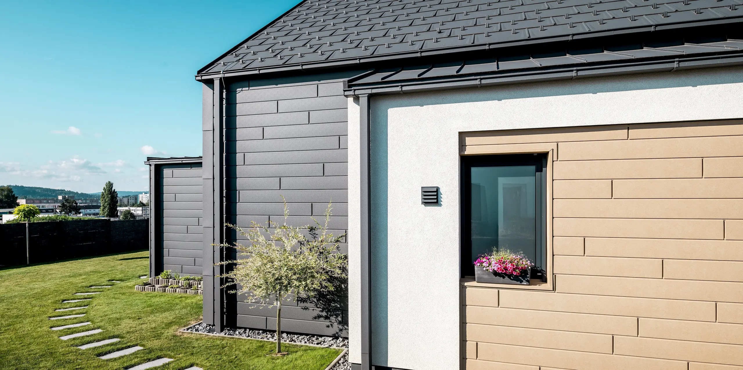 Detailansicht der PREFA Aluminium-Gebäudehülle mit Dachplatte R.16 und Sidings in P.10 Dunkelgrau und P.10 Sandbraun. Die klare Linienführung der Fassade und die kontrastreiche Farbgestaltung verleihen dem Einfamilienhaus eine moderne Optik. Die langlebigen Aluminiumoberflächen bieten zuverlässigen Schutz vor Witterung und sorgen für eine dauerhaft elegante Erscheinung.