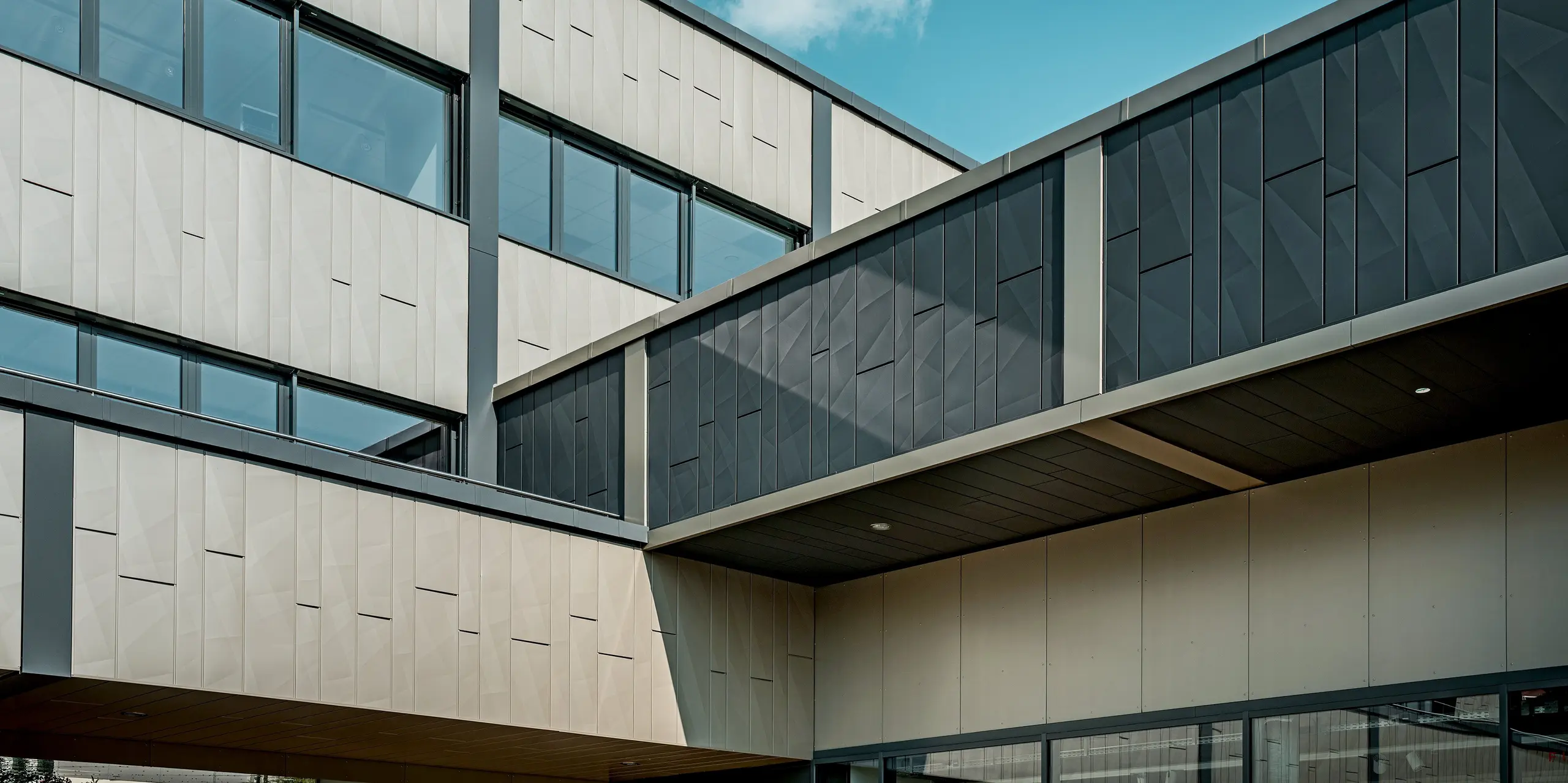 L'impressionnante façade en aluminium du centre commercial de Rohrbach a été revêtue de panneaux de façade Siding.X PREFA, de couleur bronze et anthracite. L'élégante transition entre les deux teintes est particulièrement saisissante et confère à la façade une allure dynamique et moderne. La structure épurée des éléments Siding X crée une articulation distinctive des surfaces murales. Les motifs géométriques des panneaux sont particulièrement marqués et ajoutent une impression de profondeur unique.
