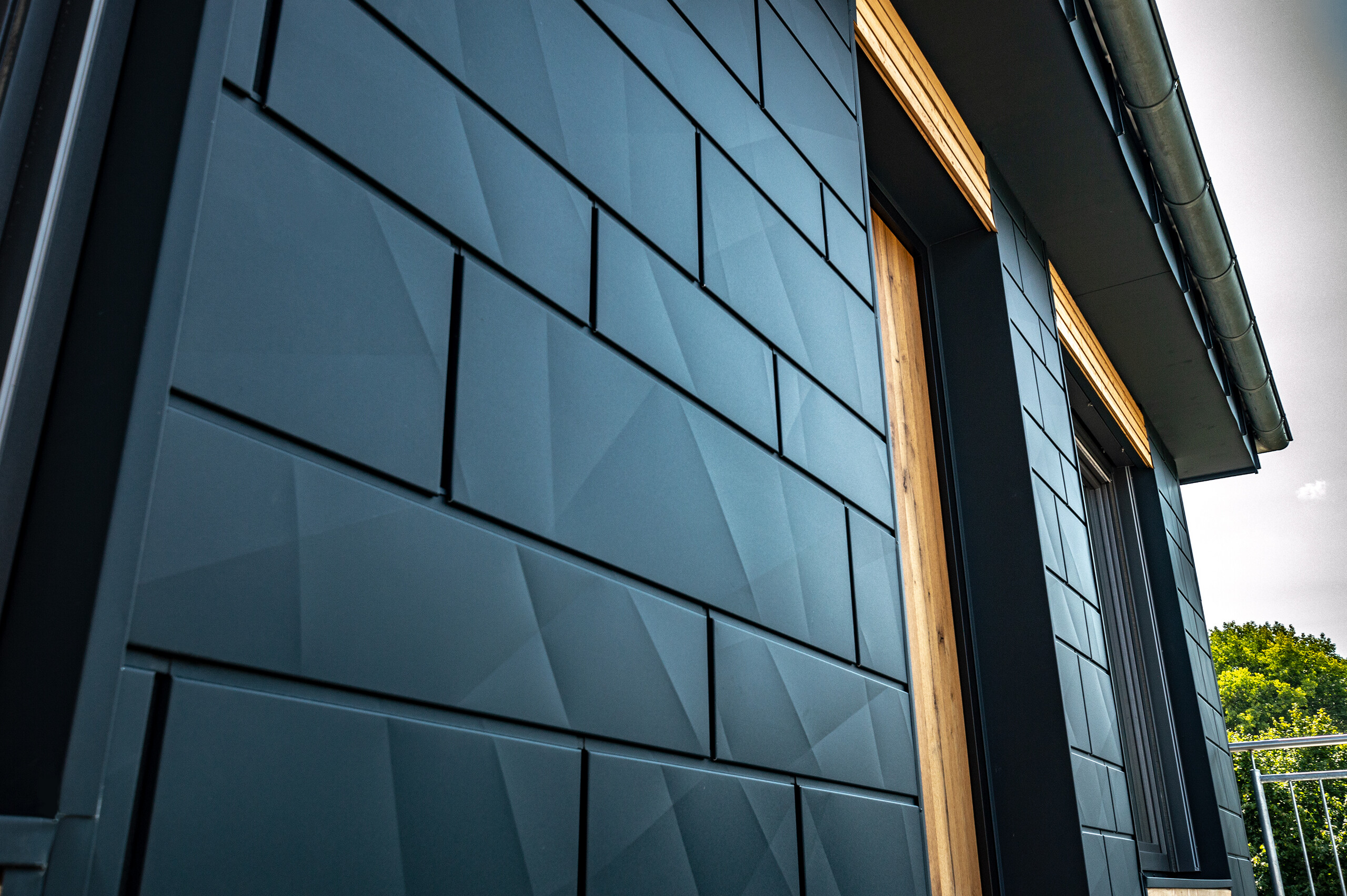 Façade avec le Siding.X PREFA en anthracite, avec portes-fenêtres et grandes baies vitrées, combinée à une façade en bois.