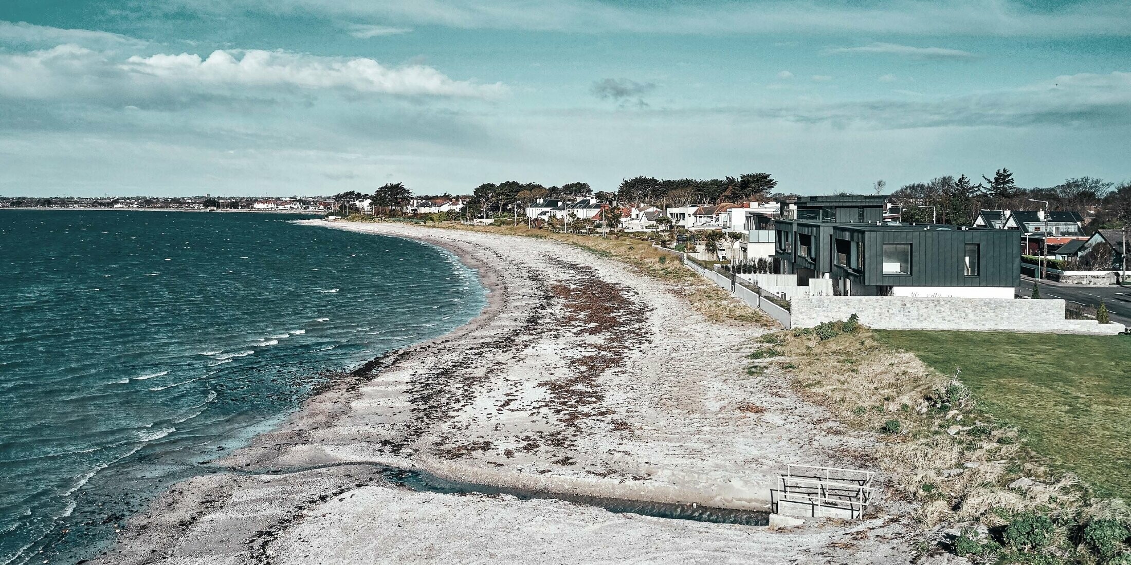 Bild der Wohnhäuser am Strand. Auf der linken Seite sieht man das Meer, auf der rechten Seite sind die Reihenhäuser zu sehen.