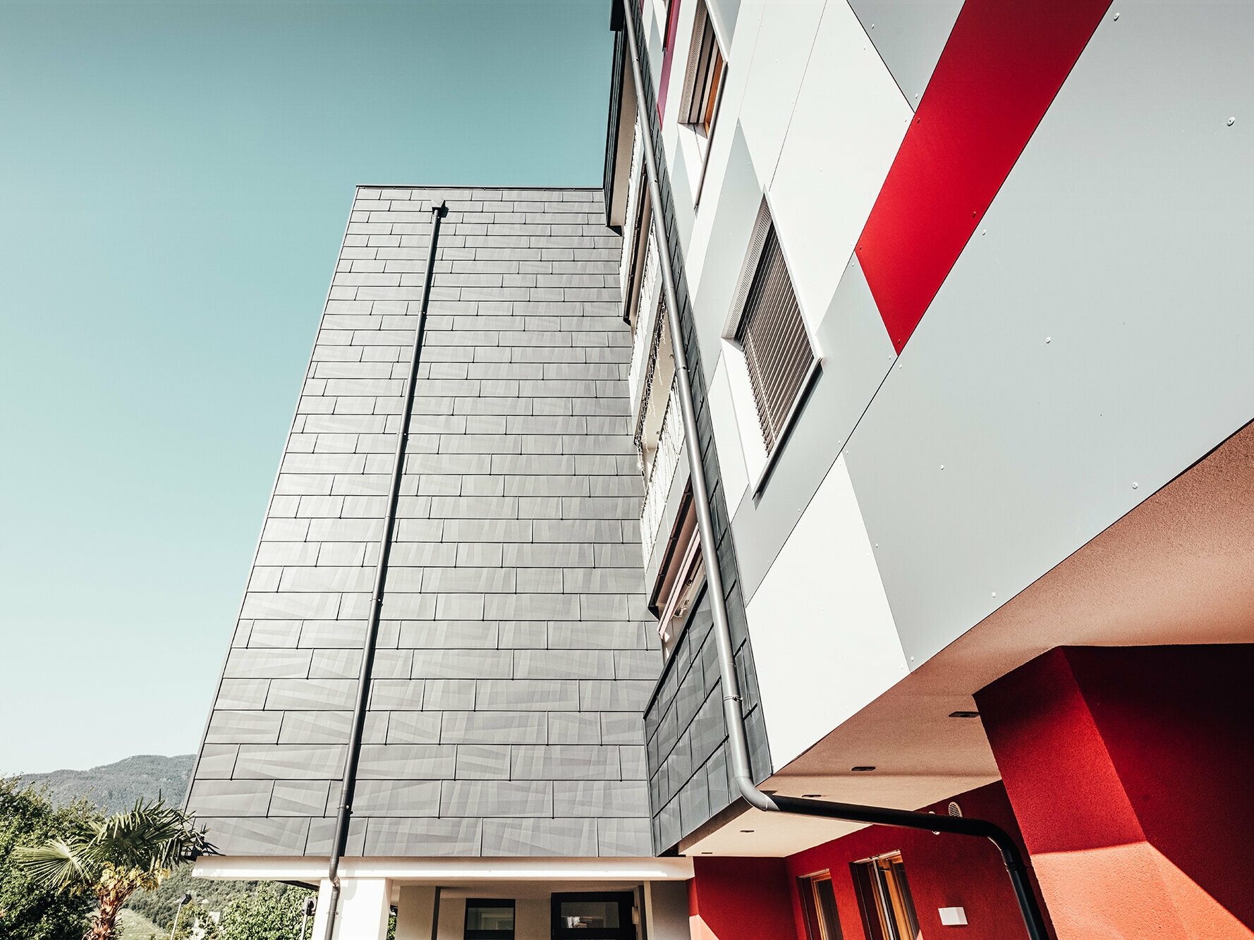 Nahaufnahme von unten. Frontal: die anthrazitfarbene PREFA Fassade. Rechts: die weiß-grau-rote Fassadenfront.