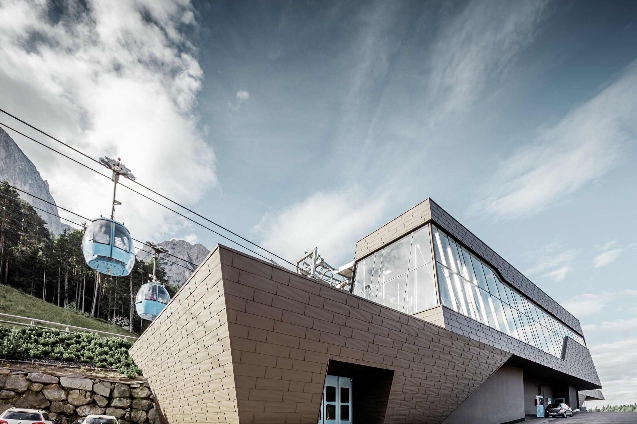 Gare de départ rénovée de la télécabine de l’Alpe di Siusi rappelant les Dolomites qui s’élèvent en toile de fond avec ses arêtes et ses surfaces irrégulières — Façade en aluminium PREFA (brun)