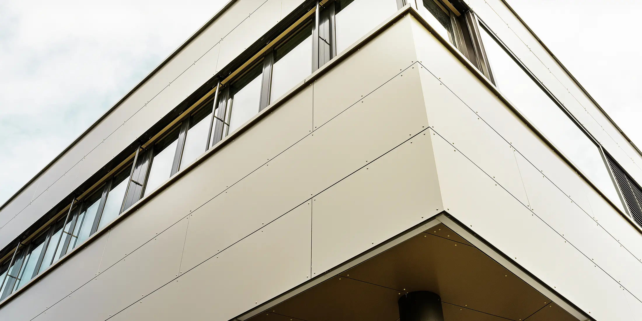 Die Eckaufnahme des Firmengebäudes in Wabern hebt die präzise montierten PREFA Aluminium Verbundplatten in Bronze hervor. Die elegante Flachdacharchitektur und die klar strukturierten Fensterflächen schaffen ein modernes, hochwertiges Erscheinungsbild.