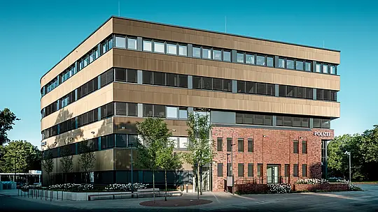 Vue extérieure saisissante du commissariat 43 à Hambourg : le nouveau bâtiment, à la structure précise, semble flotter au-dessus de la maçonnerie existante et impressionne par sa façade en aluminium PREFA, composée de profils extrudés « triangle » d’un élégant bronze moyen. La surface finement texturée crée des reflets vibrants selon l’angle de la lumière, conférant au bâtiment profondeur et dynamisme. Véritable prouesse architecturale, la façade allie design moderne et atouts tels qu’une haute résistance à la corrosion, une grande durabilité et un entretien minimal.