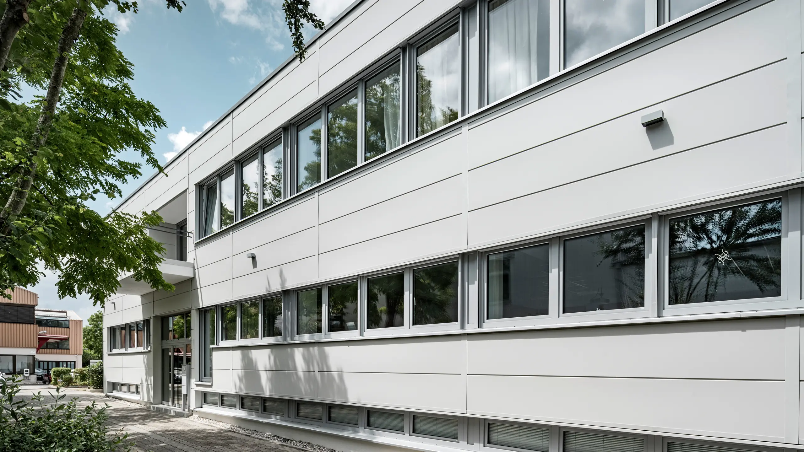Des Sidings PREFA grand format entourent un bâtiment d'entreprise à Oberschleißheim (Allemagne). Les éléments de façade extra-larges en aluminium ont été choisis dans la couleur blanc Prefa.