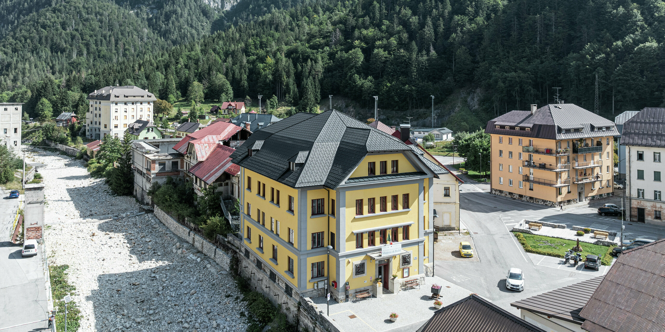 Eingebettet in eine beeindruckende Berglandschaft liegt das Museo Cave del Predil in Italien. Das Museum mit der auffallend gelben Fassade ist mit hochwertigen PREFA Dachplatten in der Farbe P.10 Anthrazit ausgestattet. Das widerstandsfähige Blechdach garantiert optimalen Schutz vor alpinen Witterungseinflüssen wie Schnee und Sturm, gepaart mit ästhetischem Design. Im Hintergrund erhebt sich majestätisch das Alpenpanorama mit dichten Wäldern und felsigen Gipfeln.