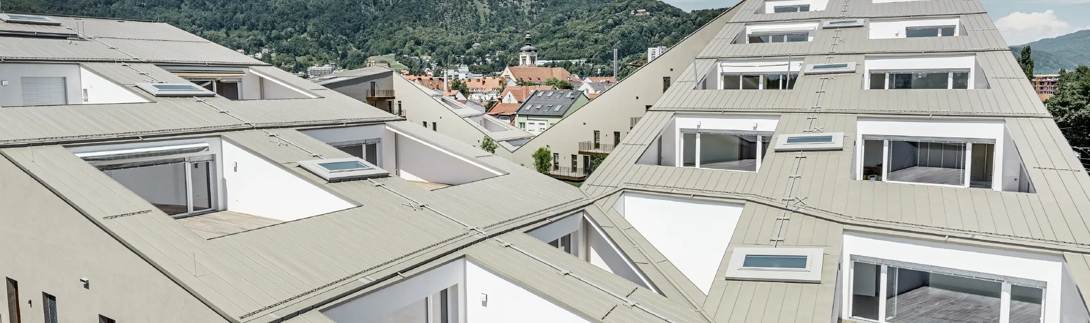 lang gezogene Wohnhausanlage in Graz mit flachen Dachflächen und integrierten Terrassen und großflächigen Fenstern mit einem Prefalzdach in der Sonderfarbe broncemetallic