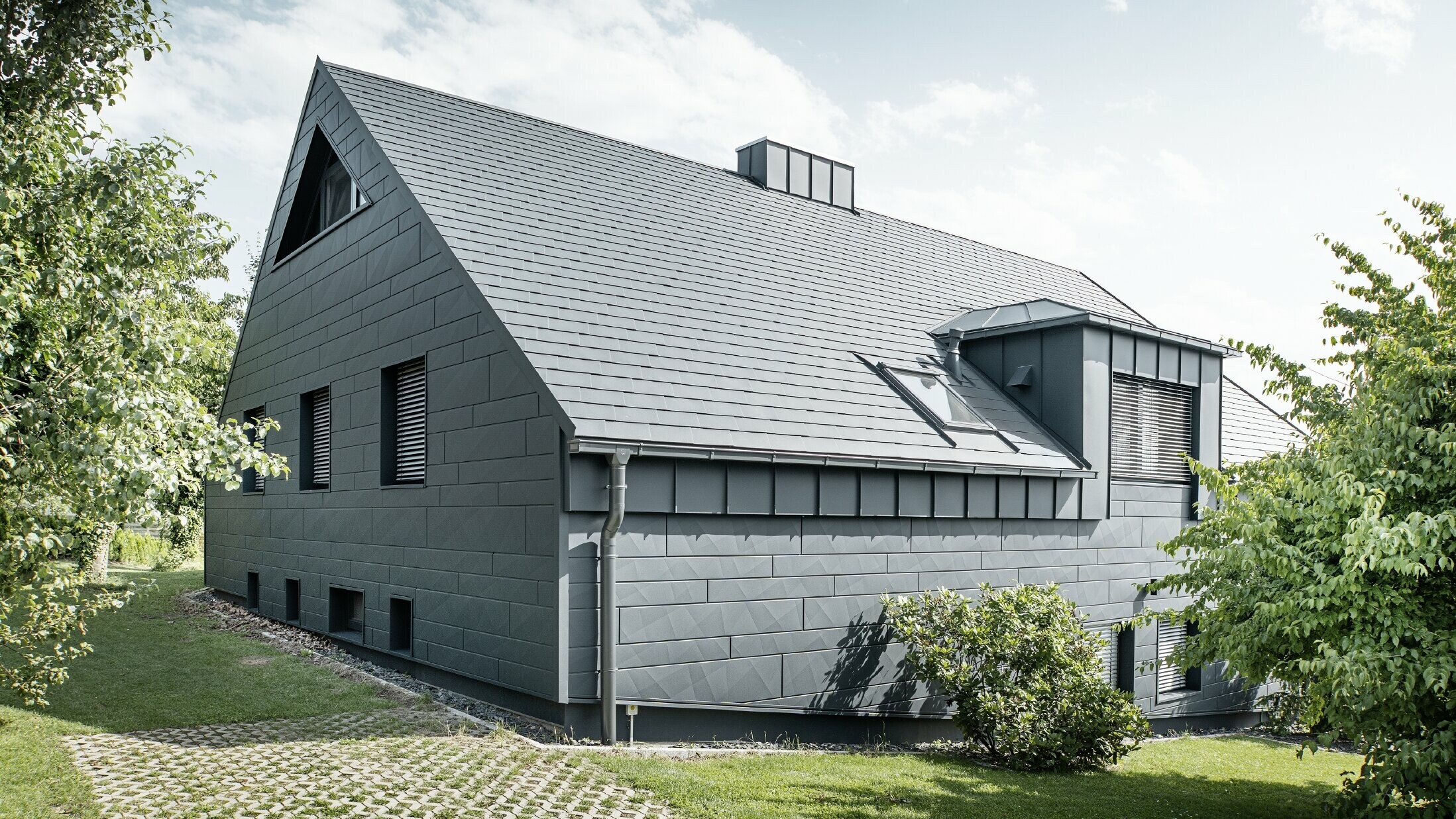 Großes Einfamilienhaus mit Satteldach und vielen Fenstern. Das gesamte Haus wurde mit einer Aluminiumhülle in Anthrazit verkleidet, am Dach kamen PREFA Alu-Dachschindeln zum Einsatz und an der Fassade Siding.X in Anthrazit.