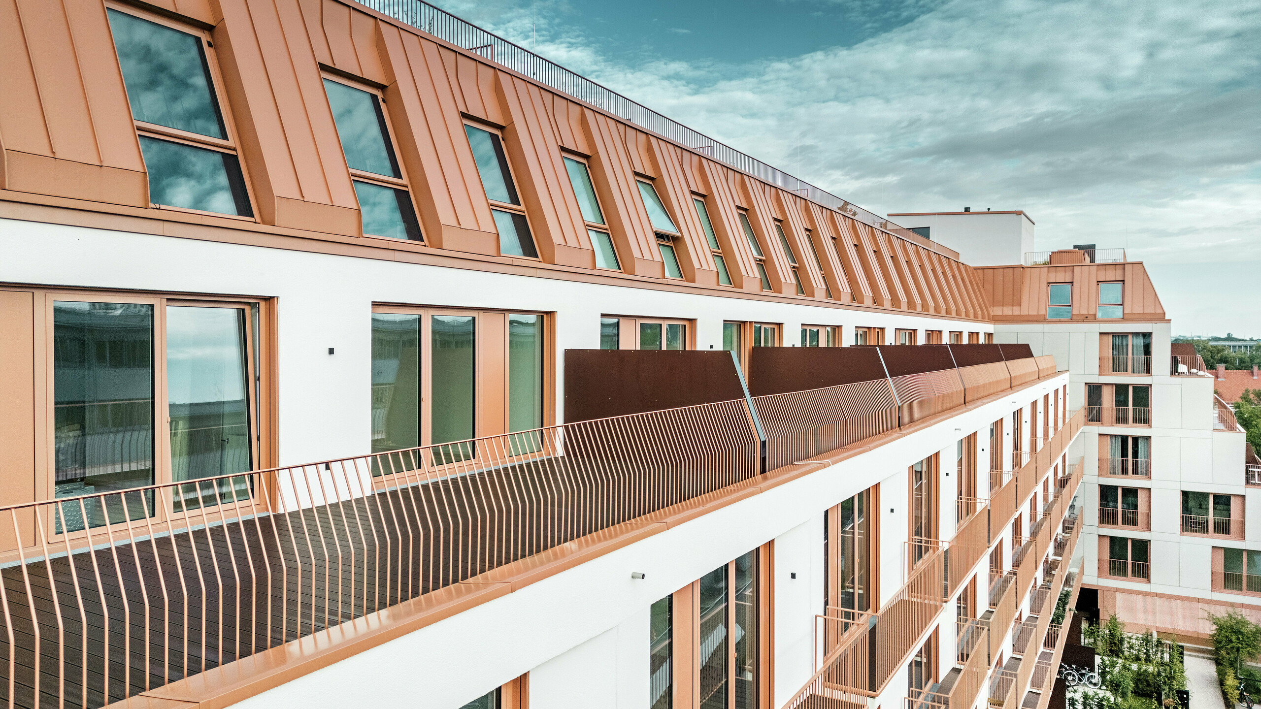 Das moderne Wohngebäude Van B in München besticht durch seine markante Dachlandschaft aus PREFALZ-Aluminium in der Sonderfarbe IGP Orange HDP. Die langlebige und wartungsarme Dachkonstruktion von PREFA gewährleistet ästhetische Integrität und hohe Witterungsbeständigkeit. Die elegante Fassadengestaltung mit kupferroten Fensterrahmen und großzügigen Balkonen unterstreicht das innovative Architekturkonzept. Die ideale Lösung für urbane Bauprojekte mit hohen Ansprüchen an Design und Funktionalität.