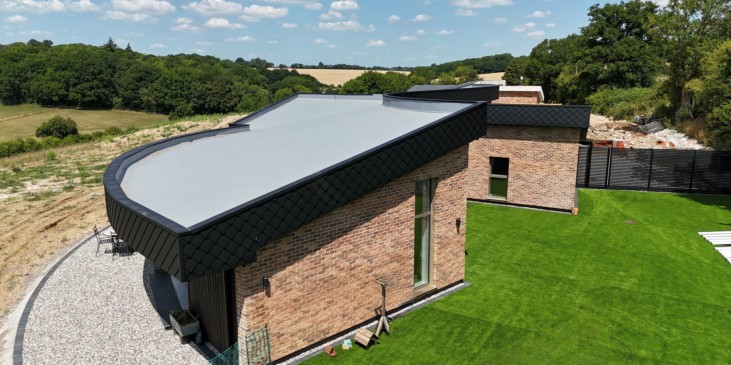 Dieses moderne Einfamilienhaus stammt aus dem Wohnprojekt „Doone Brae Farm“ und besticht durch seine markante Gebäudeform. Die Klinkerfassade wird im oberen Bereich von PREFA Wandprofil 20 × 20 in Anthrazit abgelöst. Das Eco House ist in eine grüne Landschaft eingebettet.