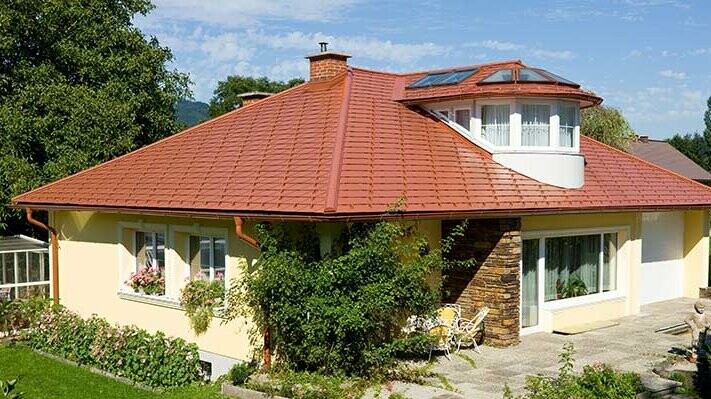Maison individuelle avec toit à croupes et lucarne recouverte avec le bardeau PREFA en aluminium imitation tuile, rouge tuile.