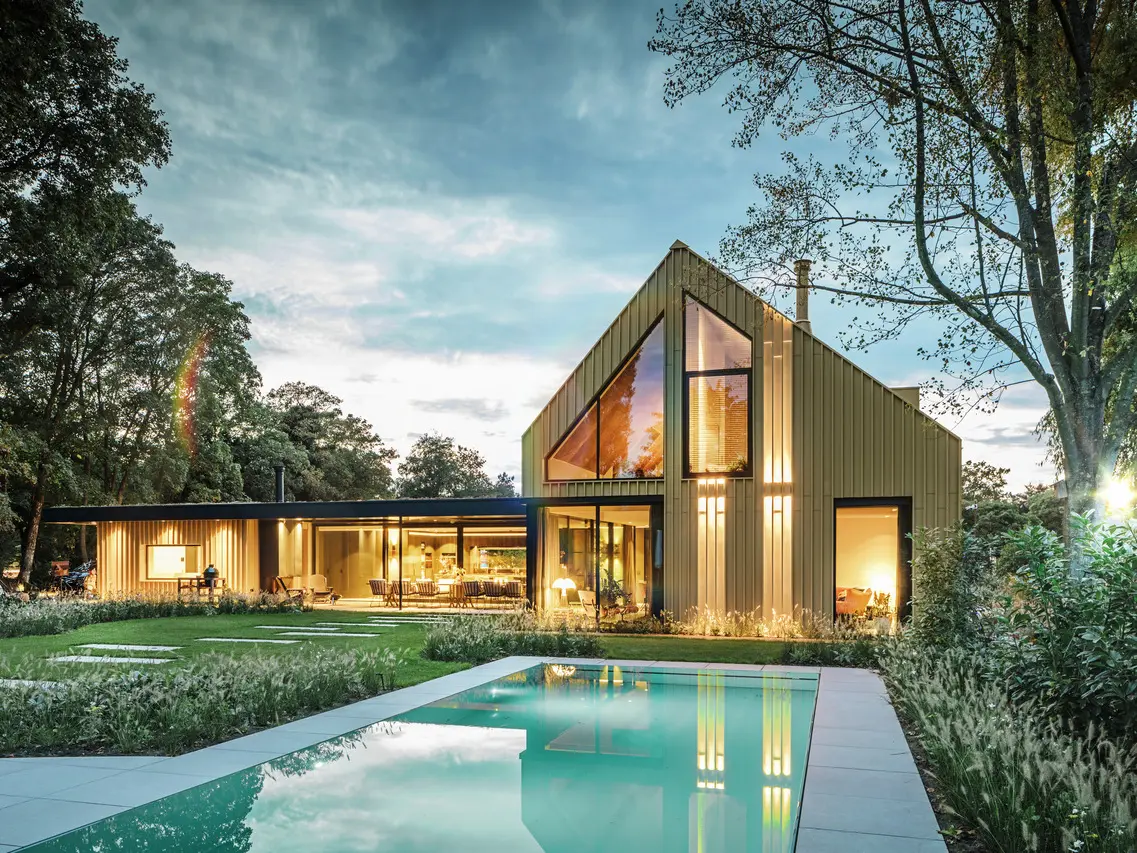 Vue de la maison individuelle d'Elst recouverte en Prefalz et Falzonal. La maison est entourée d'arbres et une piscine est visible au premier plan.