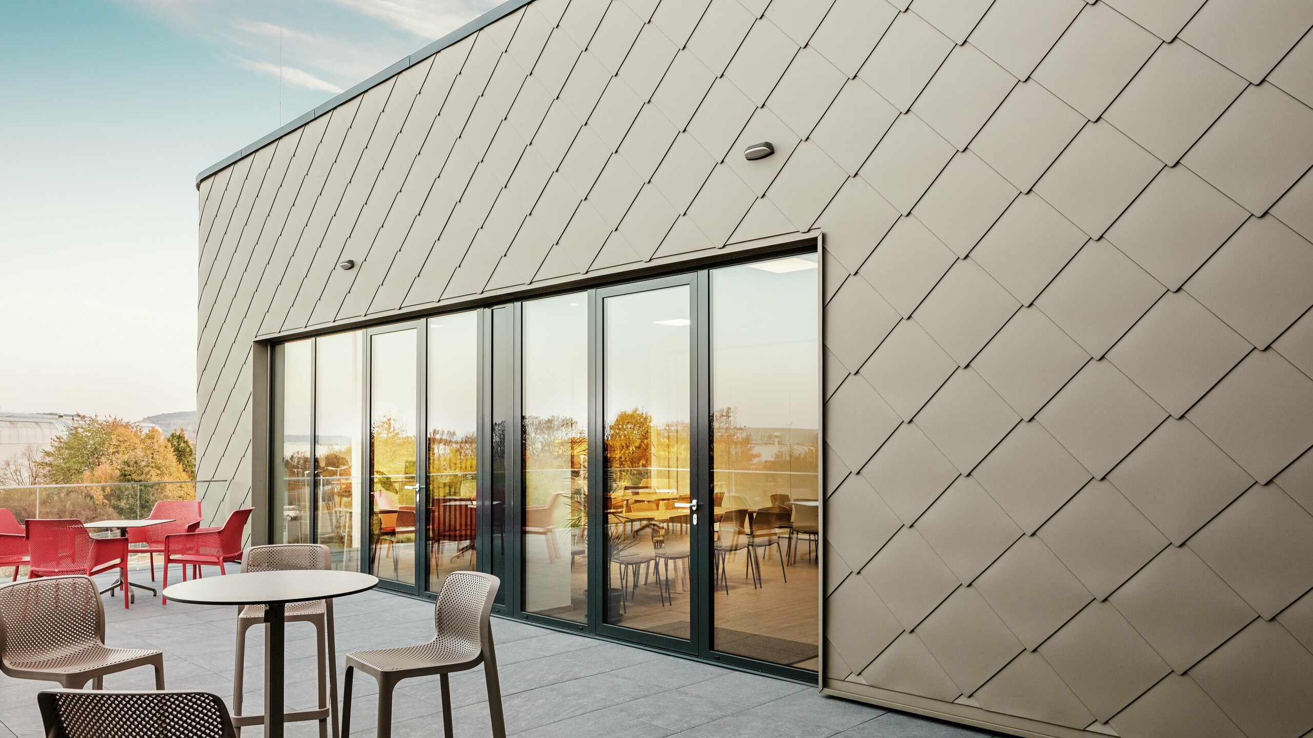 La façade du nouveau site PREFA à Törökbálint impressionne par les élégants losanges de façade PREFA 44 × 44 en P.10 bronze prefa. La façade en aluminium posée avec précision crée une apparence moderne et dynamique tout en offrant une protection maximale contre les éléments. La généreuse façade vitrée relie les espaces intérieurs et extérieurs et crée une atmosphère lumineuse et accueillante sur la terrasse spacieuse.